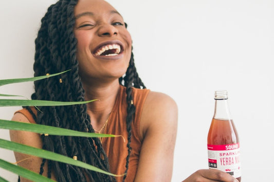 woman laughing and holding a yerba tea bottle